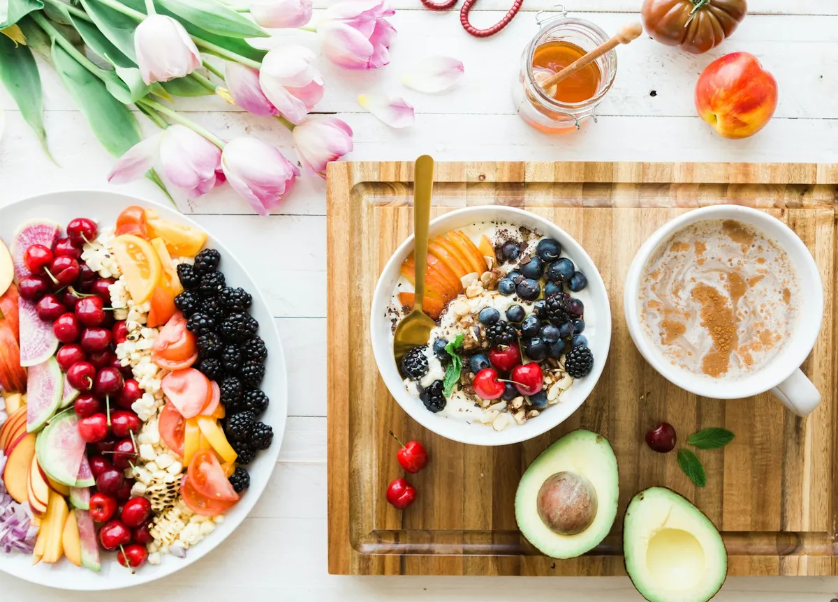 A breakfast table seen from above: a bowl of yoghurt with berries and peach, a coffee, cherries and avocado