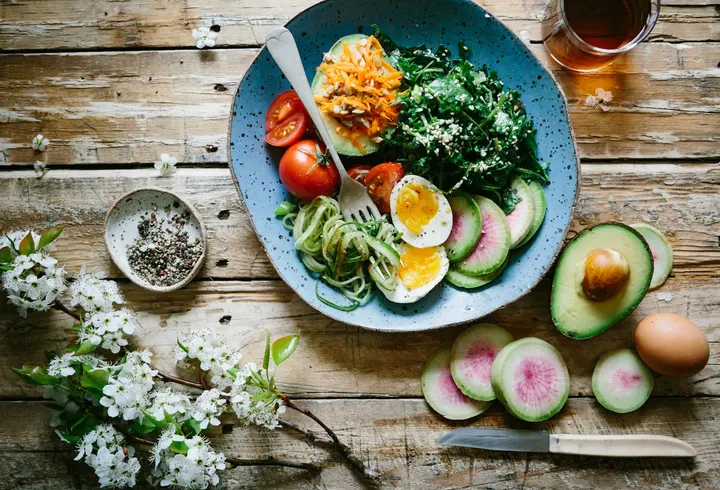 A blue bowl with spinach, a soft-boiled egg, tomatoes and avocado on a wooden table