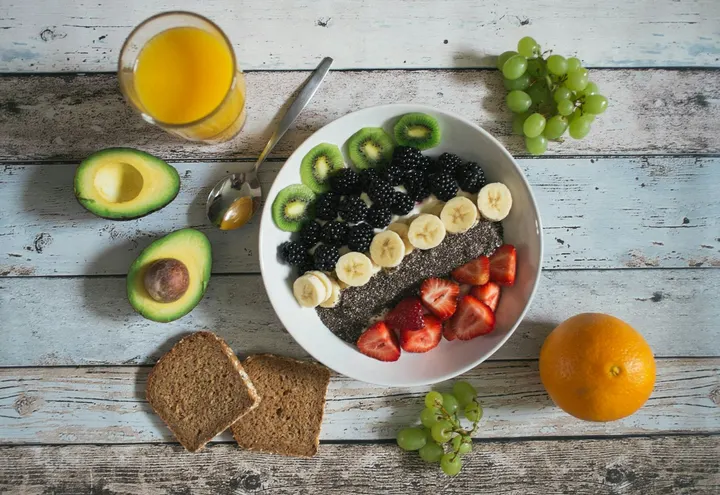 A fruit bowl with kiwi, blackberries, banana and strawberries beside wholegrain toast, avocado and orange juice
