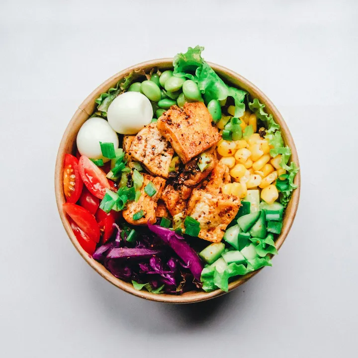 A colourful bowl of tofu, edamame, corn, tomatoes, cucumber and red cabbage
